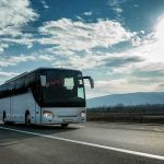 Alpine Tour Bus Horror – Dozens Down White coach bus driving on a highway under a bright sky