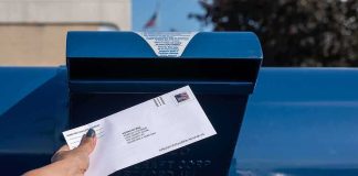 High Court Slams Brakes On Ballot Barcodes Hand mailing an envelope into a blue postal box