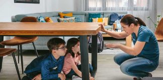 adult teaching two children to take cover under a table