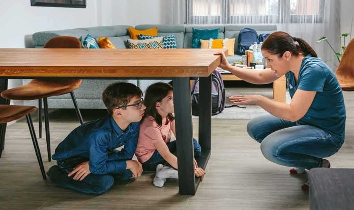 adult teaching two children to take cover under a table