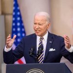 Joe Biden speaking at a podium with microphones and U.S. flags behind him