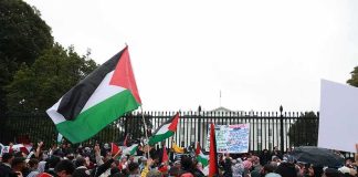 Tour Opener Turns Political Flashpoint Crowd holding flags and signs outside a fenced government building