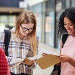 Mandatory Outing Policies Hit Legal Wall Students smiling while reading papers in a school hallway