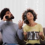 Couple on a couch reacting to water leaking from the ceiling