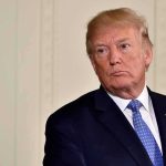 Gold-Plated Outrage: Trump Statue Inside Donald Trump in a dark suit with blue tie looking to the side