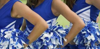 Cheerleader Clash Explodes at Rock Show Cheerleaders in blue and white uniforms holding pom poms