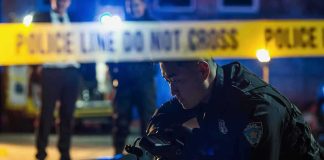 2 Killed as Chaos Erupts at Block Party Police officer examines evidence at night behind caution tape