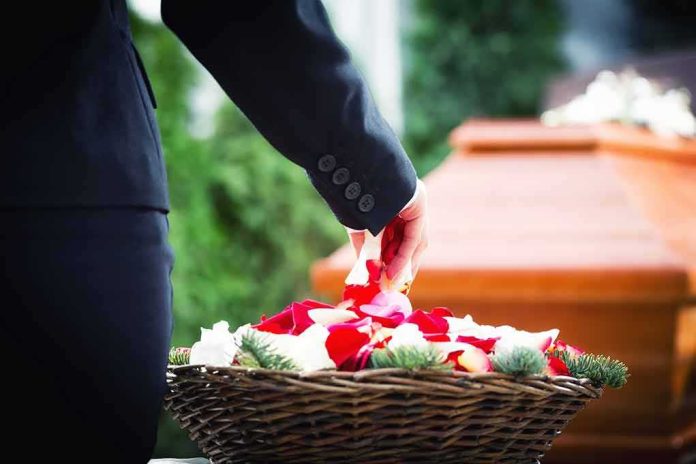 shutterstock_369951368 Person in black suit placing rose petals from basket near coffin
