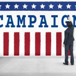Awkward Reunion: Obama Meets His Critic Man in suit writing on large campaign banner with stars and stripes