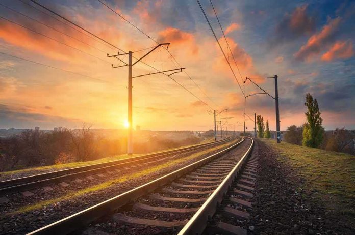 shutterstock_513158971 Curved railway tracks under power lines at sunrise