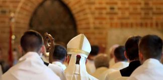 Paperwork Glitch Sends Priest Toward Combat Bishop in white mitre among clergy during church procession