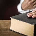 Cease-And-Desist Bomb Hits Senate Fight Hand on a thick black hardcover book on a wooden table