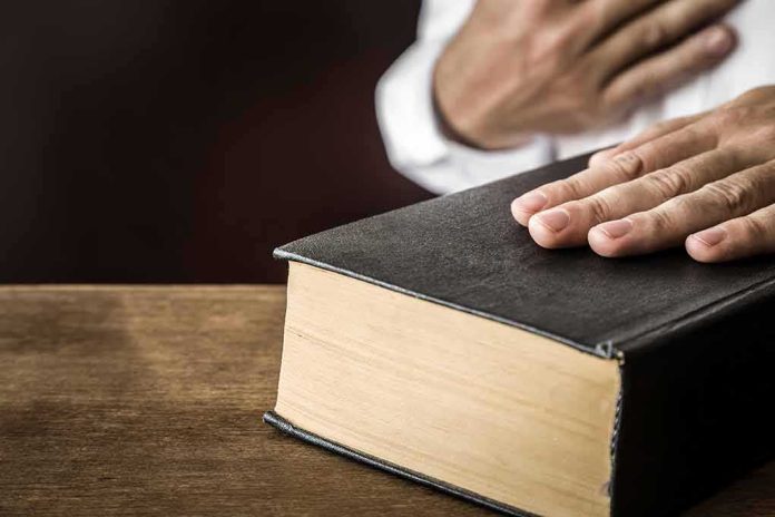 Hand on a thick black hardcover book on a wooden table